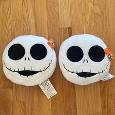 two pillows with faces on them sitting on a wooden floor, one is white and the other has black eyes