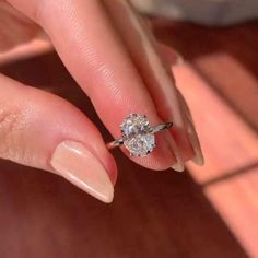 a woman's hand holding a diamond ring on her finger, with the top half of