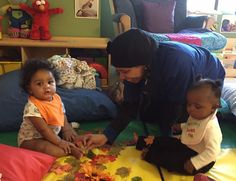 a woman and two children playing with leaves on the floor in a room full of toys