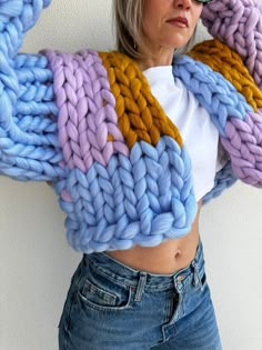 a woman is wearing a colorful knitted sweater and jeans with her hands on her head