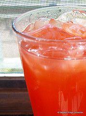 a drink in a glass with ice and garnish on the rim next to a window