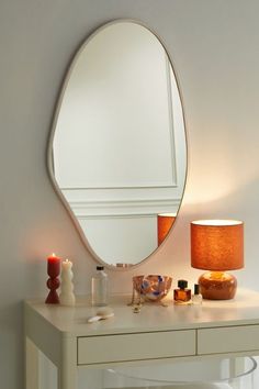 a white table with a mirror and candles on it next to a wall mounted lamp