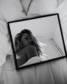 a black and white photo of a woman's reflection in a mirror on a bed