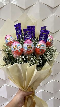 a hand holding a bunch of chocolate eggs with flowers in the middle and candy wrapped around it