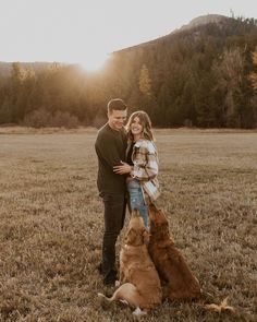 a man and woman standing next to each other in a field with two dogs sitting on the ground