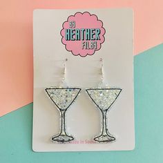 the glitter martini earrings are on display in front of a pink and blue background