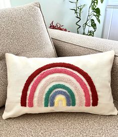 a white pillow with a rainbow embroidered on the front and side of it sitting on a couch