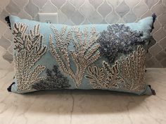 a decorative blue pillow with silver sequins and seaweed on the front, sitting on a marble countertop