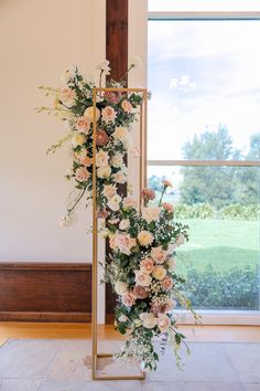 an arrangement of flowers on a gold stand in front of a window at a wedding