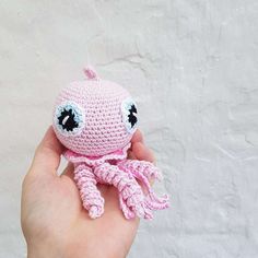 a hand holding a pink crocheted stuffed animal with black eyes and an octopus tail