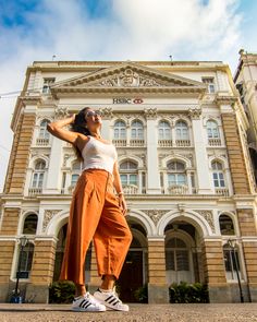 a woman standing in front of a building with her hand on her head and looking up at the sky