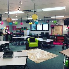 an empty classroom with tables, chairs and lights hanging from the ceiling in front of windows