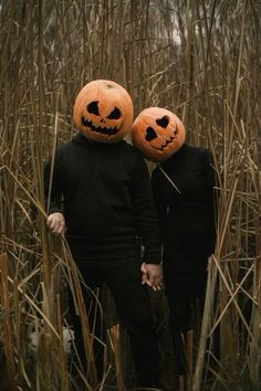 two people wearing pumpkin heads standing in tall grass