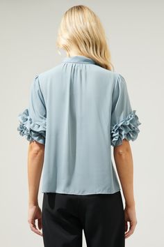 Add some fun to any office look with the Sea Mist Lida top. A blue grey chiffon shapes the Lida Top, featuring a mock, tie neck with gathered details. Ruffle layered quarter sleeves add a fun flair to a classic style blouse. Pair the look with sleek trousers and loafers for an elevated look.- Tie neck- Ruffle layered sleeves- Flowy fit- Color: GreySize + Fit - Model is 5'8" and wearing size XS- Measurements taken from size S - Chest: 19 1/4"- Length: 24 1/2" Fabric Self: 100% Polyester Style Num Light Blue Short Sleeve Blouse For Fall, Fall Light Blue Short Sleeve Blouse, Ruffled 3/4 Sleeve Blouse For Work, Ruffled 3/4 Sleeve Tops For Work, Elegant Tops With 3/4 Sleeves And Ruffles, Light Blue Ruffled Tops For Work, Tie Neck Top, Bow Tie Blouse, Blue Bow Tie