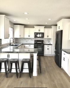 a kitchen with white cabinets, black appliances and stools on the counter top in front of an island