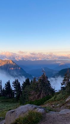 the mountains are covered in fog and low lying clouds as the sun is setting over them