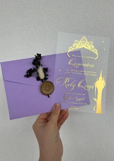 a person holding up a purple and gold wedding card with a wax stamp on it