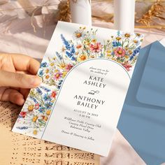 a person holding up a wedding card with flowers on it