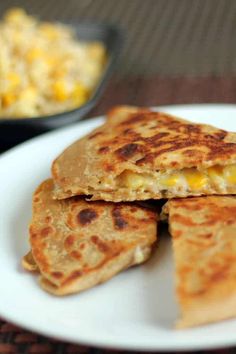 three quesadillas on a white plate next to a bowl of macaroni and cheese