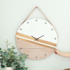 a wooden clock hanging on the wall next to a potted plant and a vase