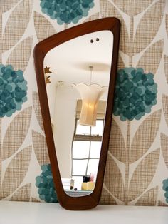 a large mirror sitting on top of a white table next to a wallpaper covered with blue flowers