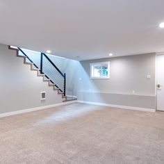 an empty living room with stairs leading up to the second floor, and carpeted floors