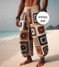 a man standing on top of a sandy beach next to the ocean wearing crocheted pants