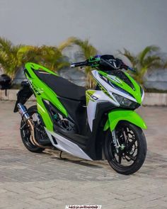 a green and white motorcycle parked on top of a brick road next to palm trees