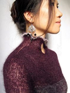 a woman with her hair in a high bun wearing a purple sweater and statement earrings