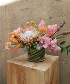 a vase filled with lots of flowers on top of a wooden block next to a wall