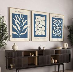 three blue and white art prints hang on the wall above a console table with vases