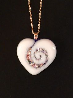 a white heart shaped pendant with a spiral design in the center on a gold chain