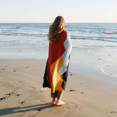 a woman is standing on the beach with her back to the camera, wrapped in a blanket