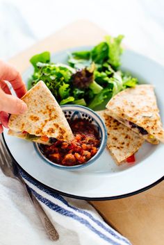 a plate with some food on it and a hand holding a piece of pita bread