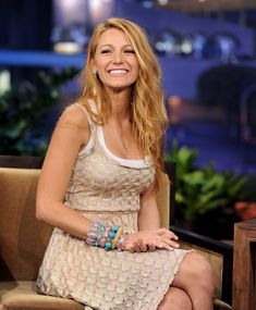 a woman sitting in a chair smiling and wearing bracelets on her left hand,