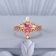 a pink diamond ring sitting on top of a white cloth covered table with a rose