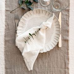 a table setting with napkins, silverware and greenery on the placemat