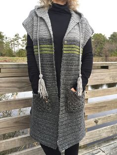 a woman standing on a wooden bench wearing a gray crochet vest with tassels