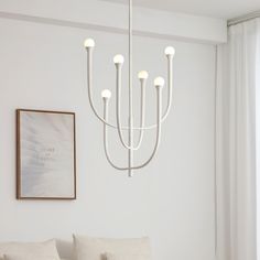 a chandelier hanging from the ceiling in a white room with pillows on the floor