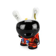 a black and white toy with an orange outfit on it's head, sitting in front of a white background