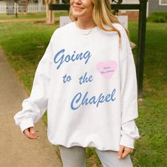 a woman standing in front of a street sign wearing a sweatshirt that says going to the chapel