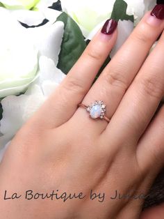 a close up of a person's hand with a ring on their finger and flowers in the background