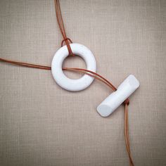 a white object is connected to a cord on a beige background with brown leather cords