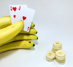 a stack of bananas with playing cards next to them on a white surface, surrounded by small stacks of banana slices