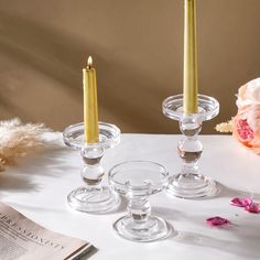 three candles are sitting on a table next to a book and some pink flower petals