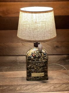 a lamp that is sitting on top of a wooden table next to a bottle with rocks in it