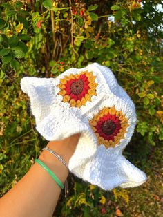 a hand holding up a white crocheted hat with sunflowers on it