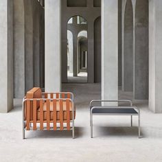 two chairs and a table in a room with concrete columns, one is orange and the other is blue