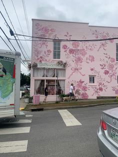 a pink building with flowers painted on it's side and people walking in front