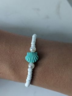 A stretchy seed bead bracelet with white beads, pearls and a aqua shell White Pearl Bracelet With Charm For Beach, White Beaded Pearl Bracelet For Beach, White Round Beads Ocean-inspired Bracelets, White Shell Beaded Strand Bracelets, White Beaded Shell-shaped Bracelets, White Stretch Bracelet With Tiny Beads For Beach, White Ocean-inspired Round Bead Bracelets, Handmade White Stretch Strand Bracelet, Ocean-inspired White Round Bead Bracelets